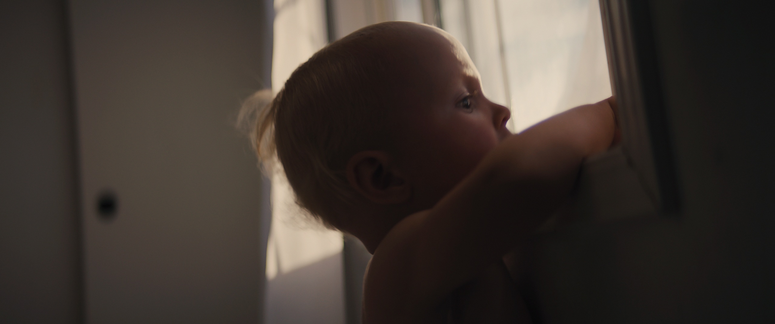 The Golden Hour — a baby at a window gazing out into the light, film still written and directed by Zane Ra